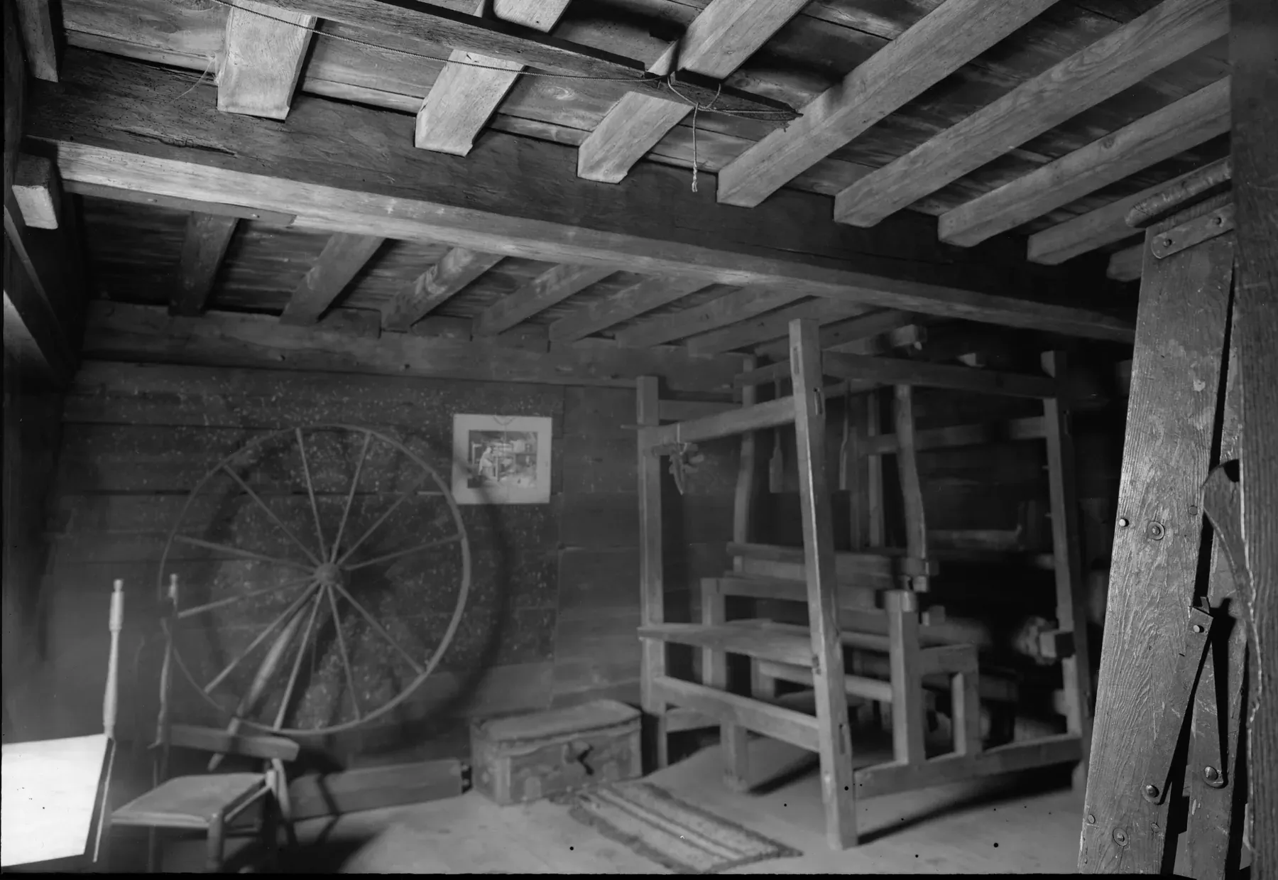 Second-floor workroom of the Fairbanks House with exposed hand-hewn ceiling joists, a loom, a spinning wheel and a plank floor