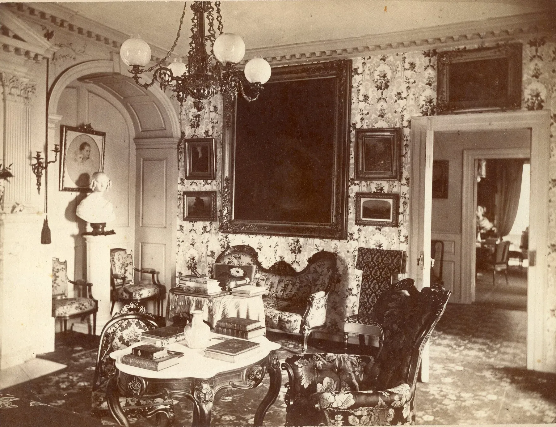 1871 photograph of the Longfellow House parlor with floral wallpaper, a gas chandelier, upholstered chairs and a patterned carpet covering the whole floor