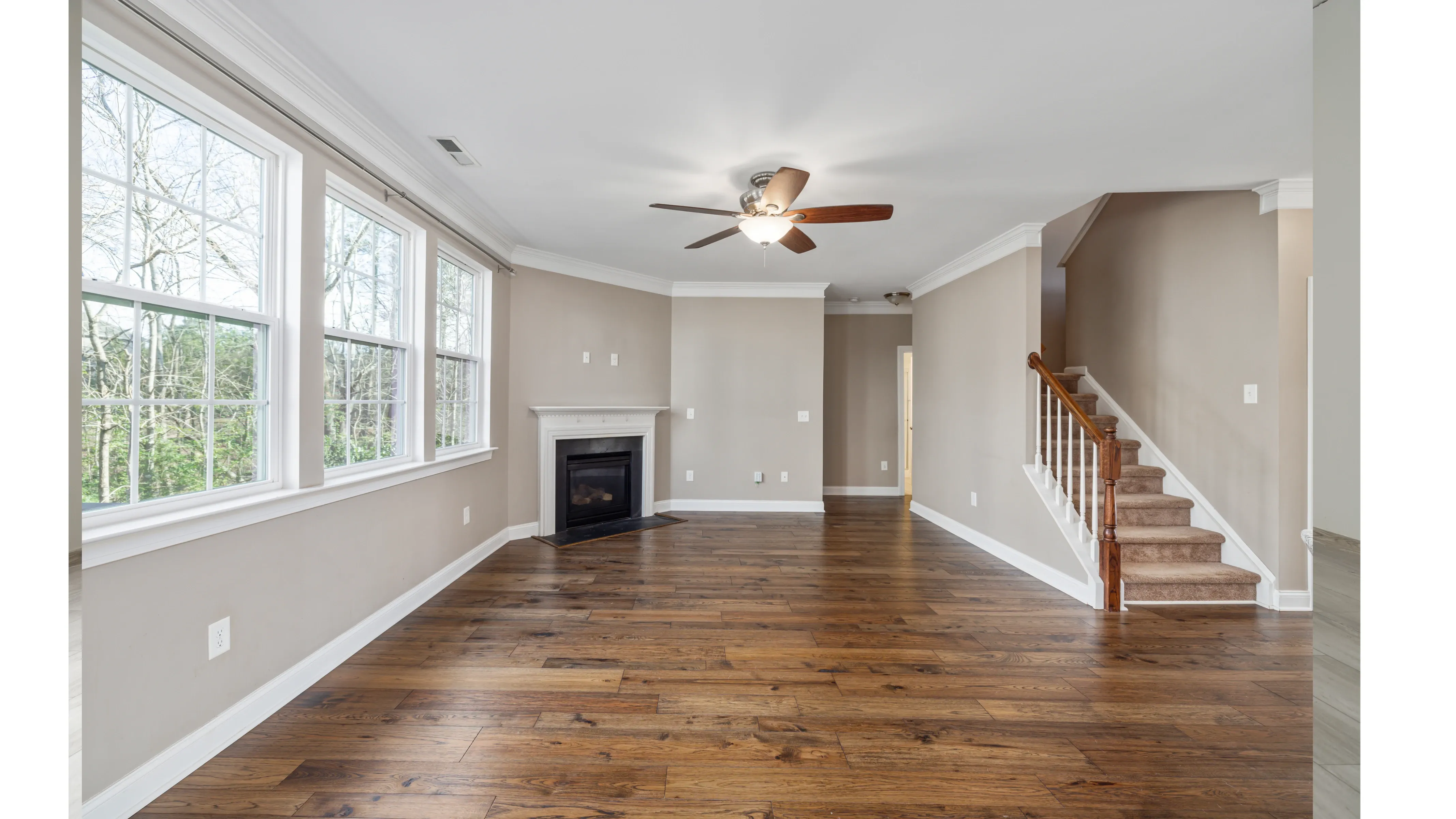 Empty living room with wide-plank hardwood flooring, a corner fireplace and a staircase to one side