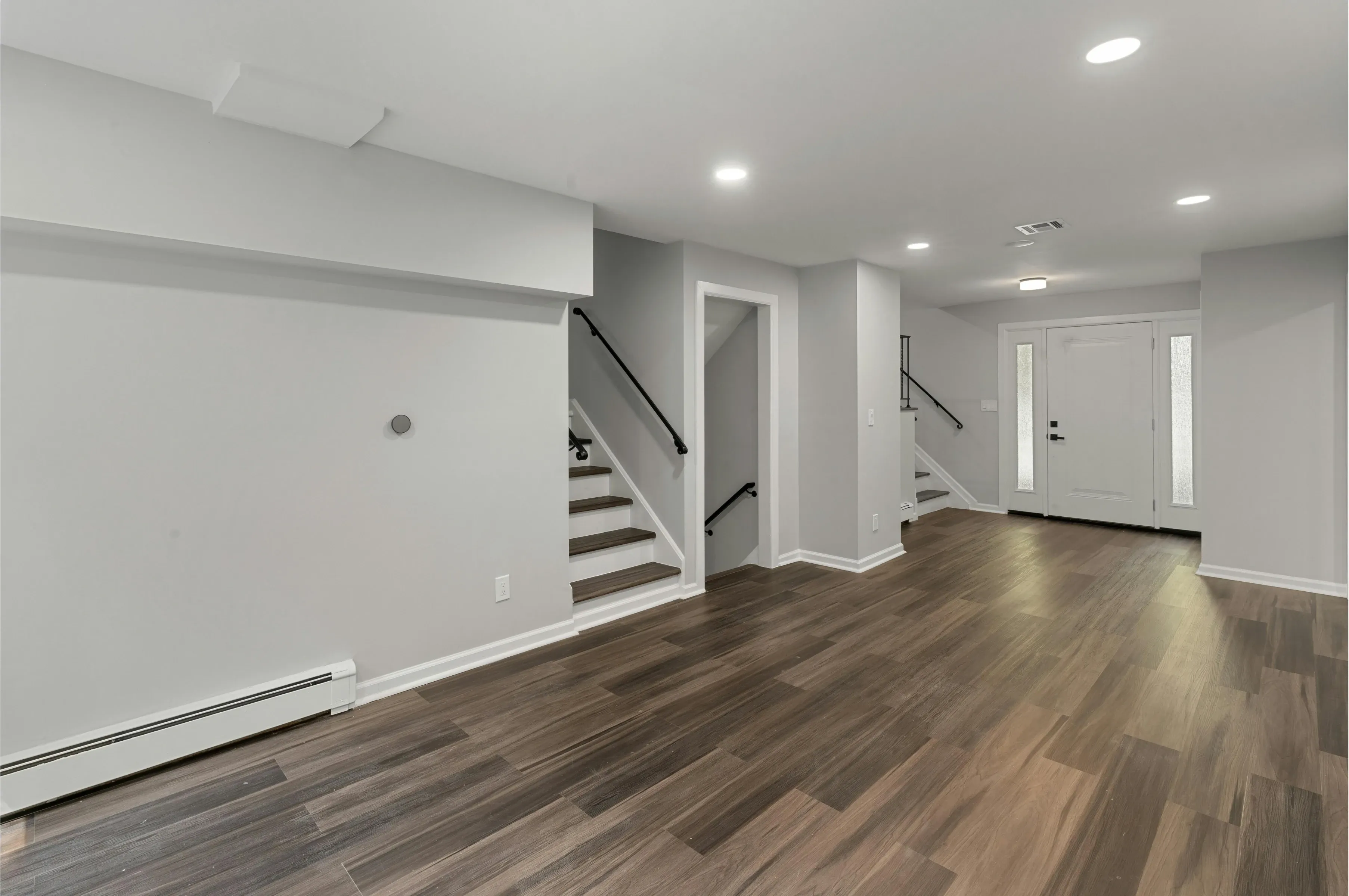 Empty finished room with dark wood-look plank flooring running from a staircase to a white front door