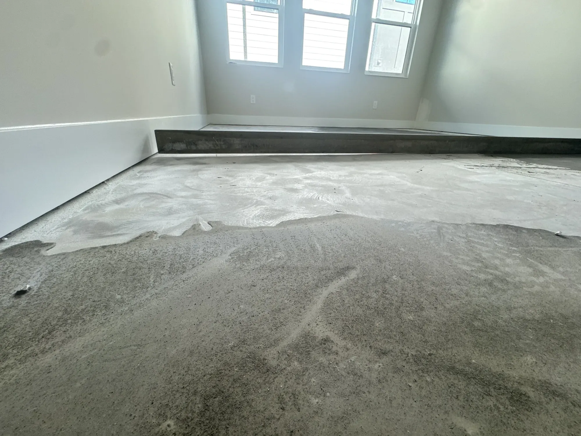 Bare concrete slab with leveling compound partly spread across it, in an empty room before installation