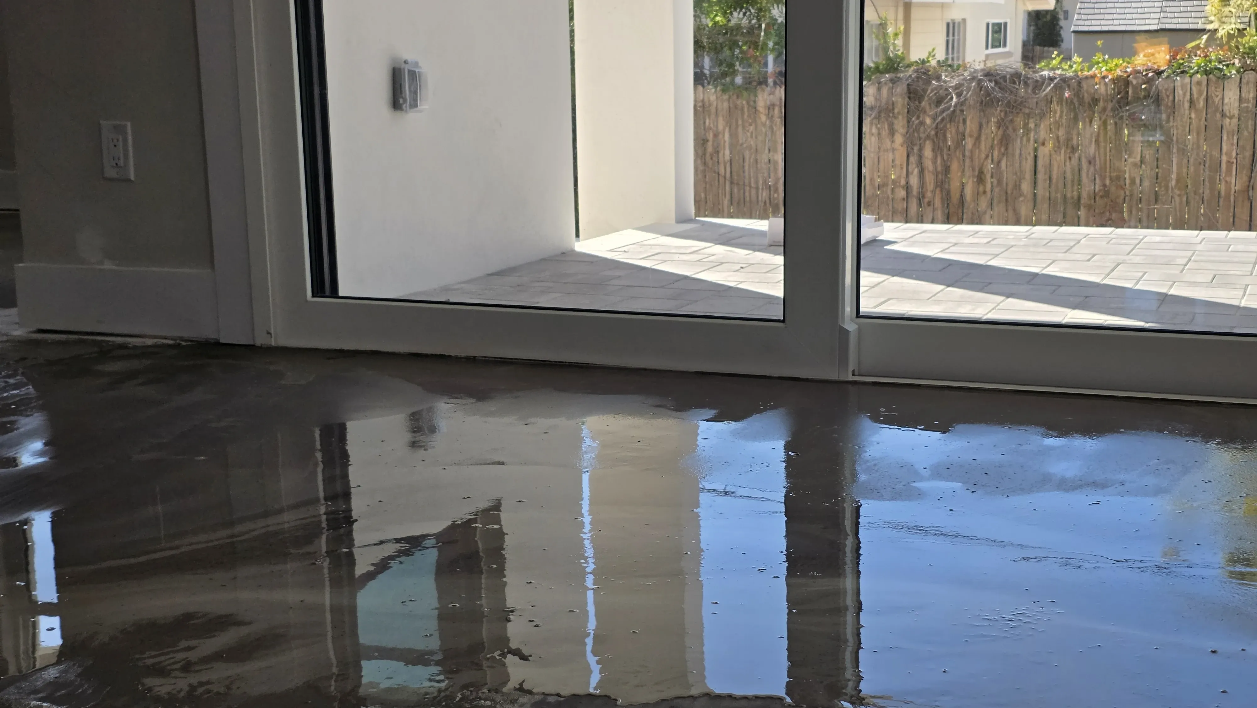 Freshly poured self-leveling compound, still wet across the slab, in front of sliding glass doors onto a paver patio