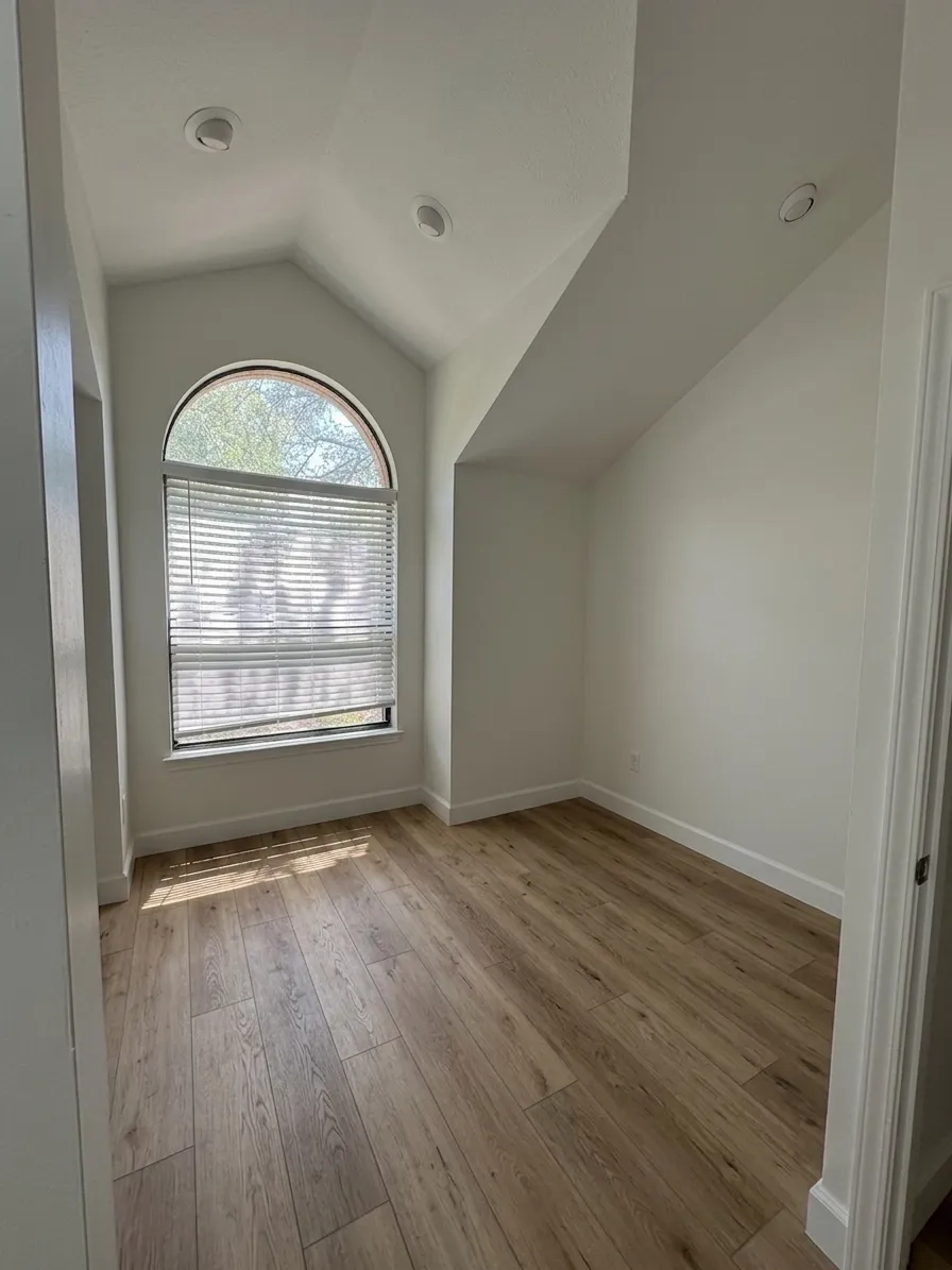 The same walk-in closet rebuilt and finished, with light wood-look vinyl plank flooring and the arched window restored