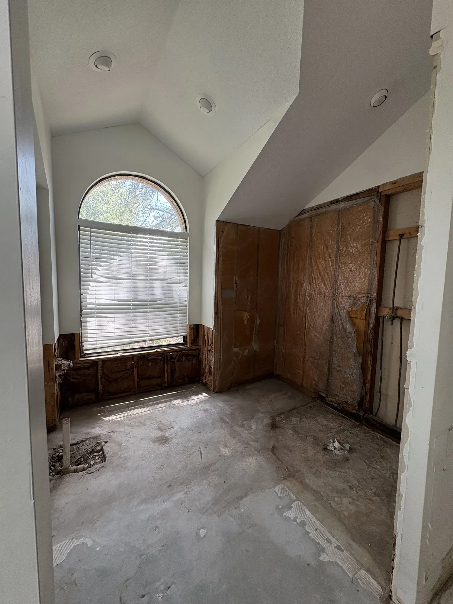 Walk-in closet stripped after water damage, with drywall cut back to waist height, the vapour barrier exposed between the studs and a plumbing stub coming out of the slab