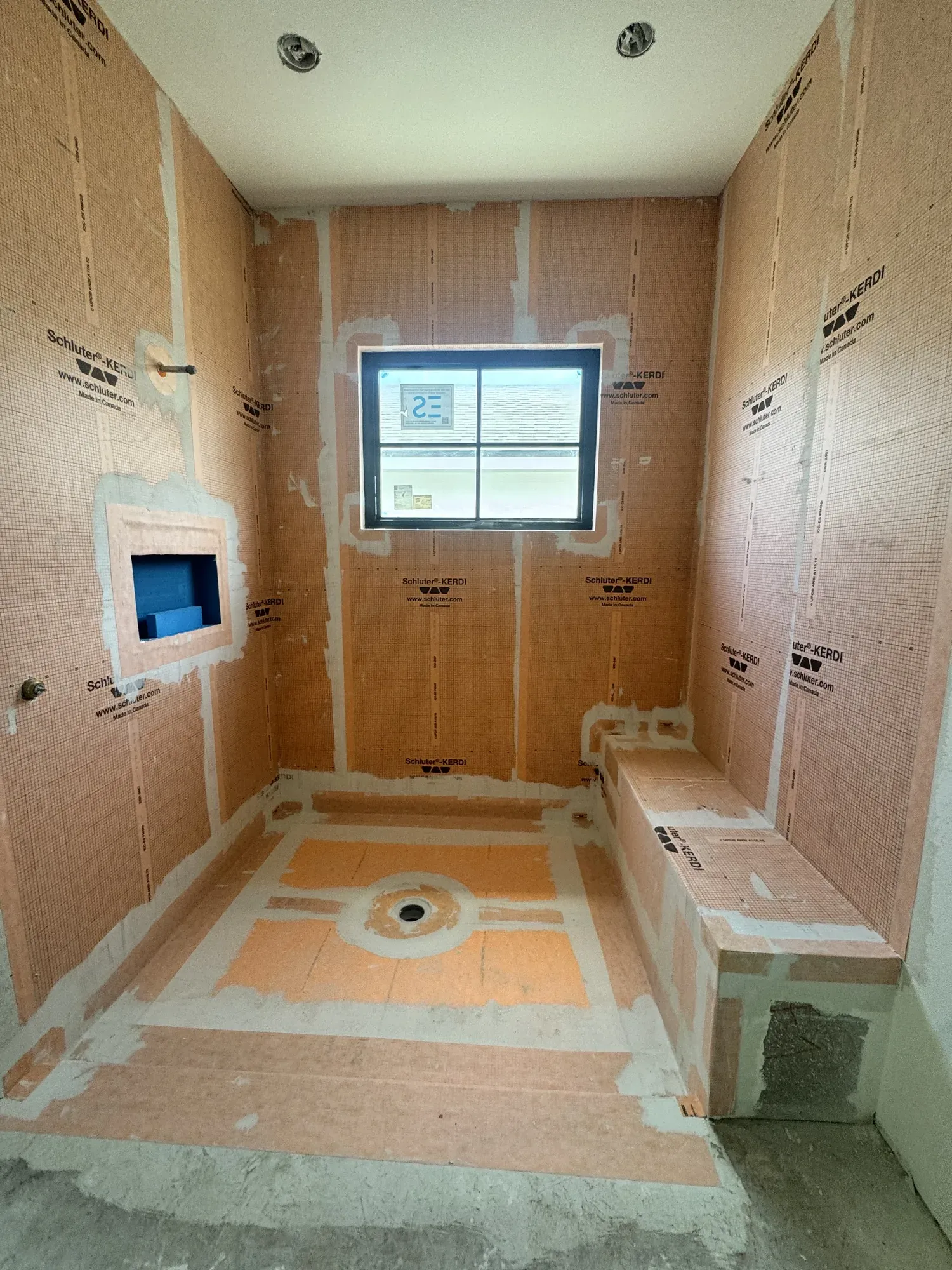 Shower fully waterproofed before tiling, with membrane over the walls, the bench and the niche, and a sloped pan with its drain