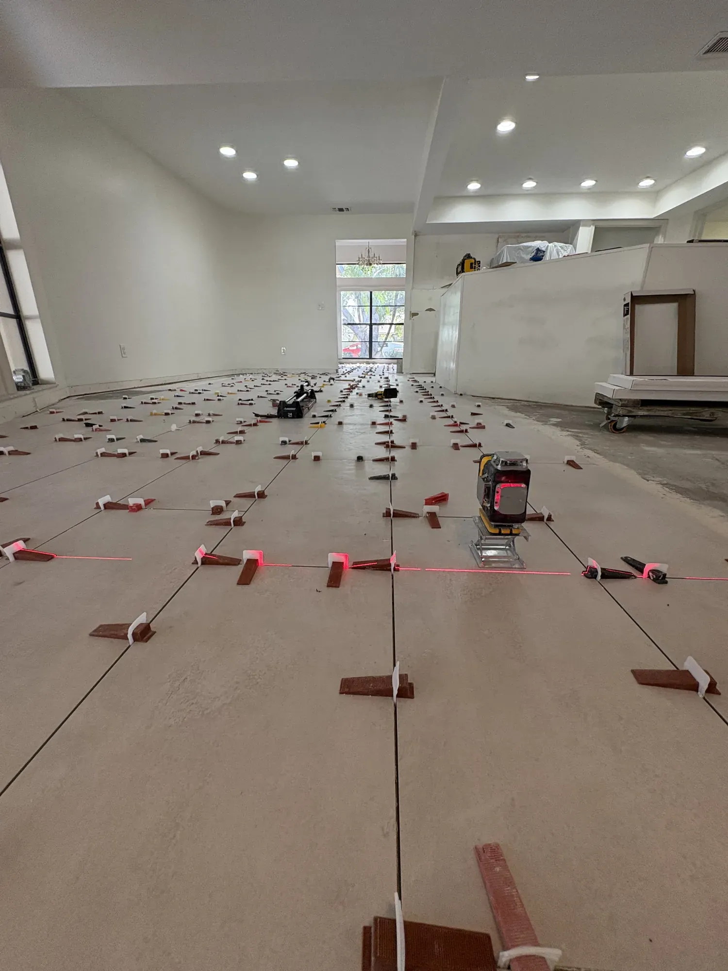 Large-format tile going down across an open living area, with levelling clips and wedges in place and a cross-line laser marking the layout