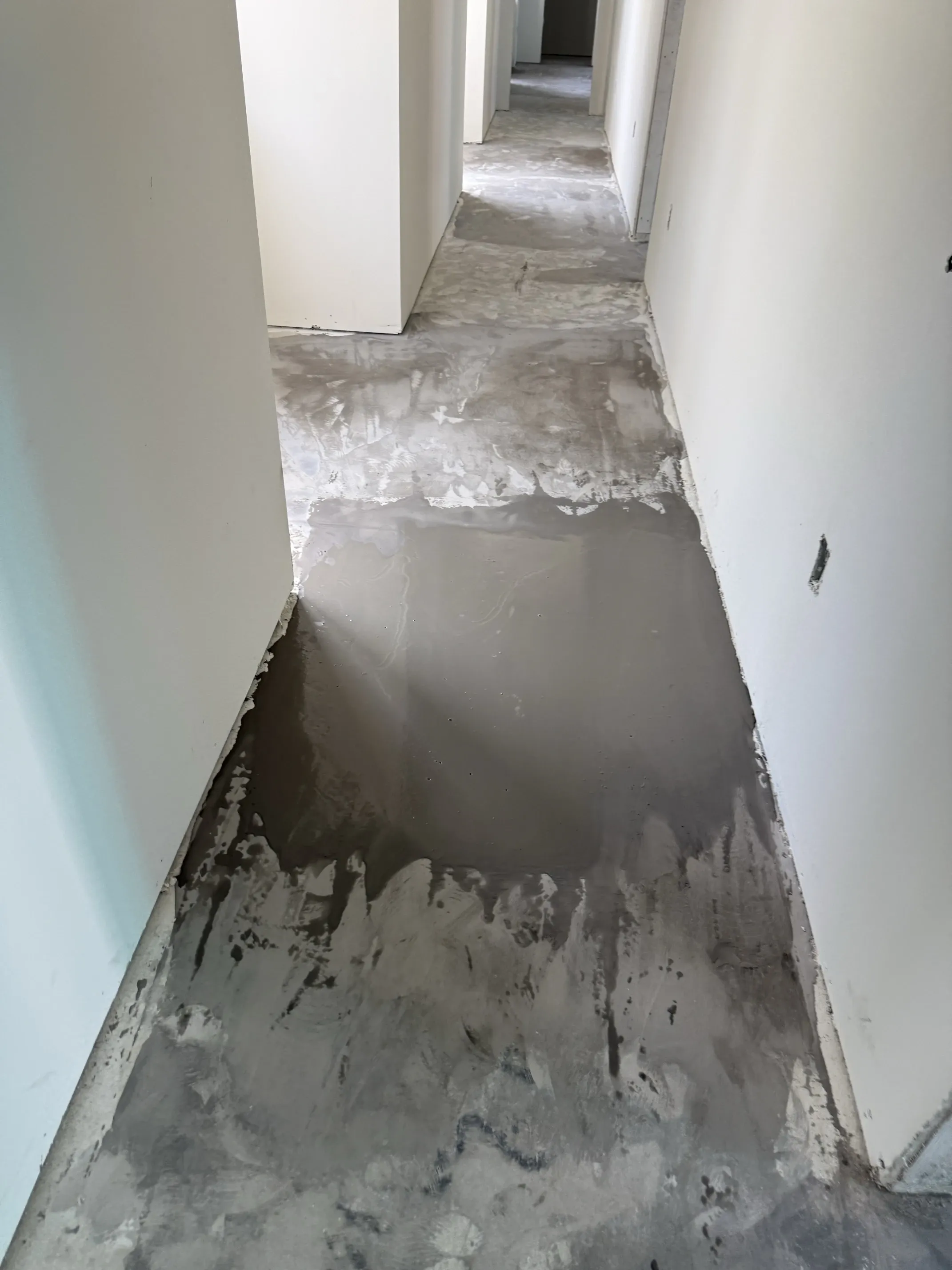 Hallway with levelling compound freshly spread over the bare slab, still wet, running between two rows of doorways