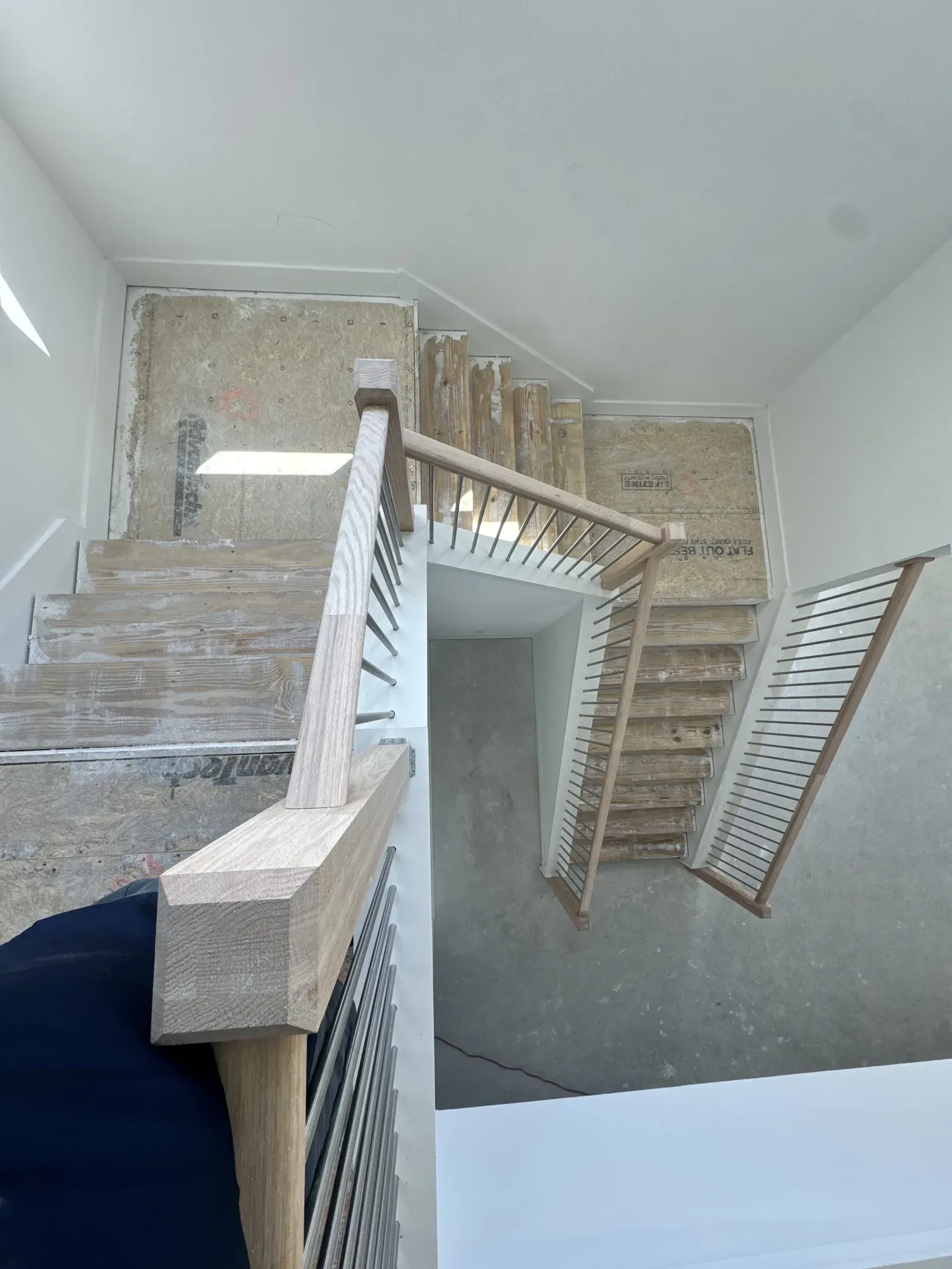 Staircase with bare plywood treads and an unfinished landing, seen from the top step