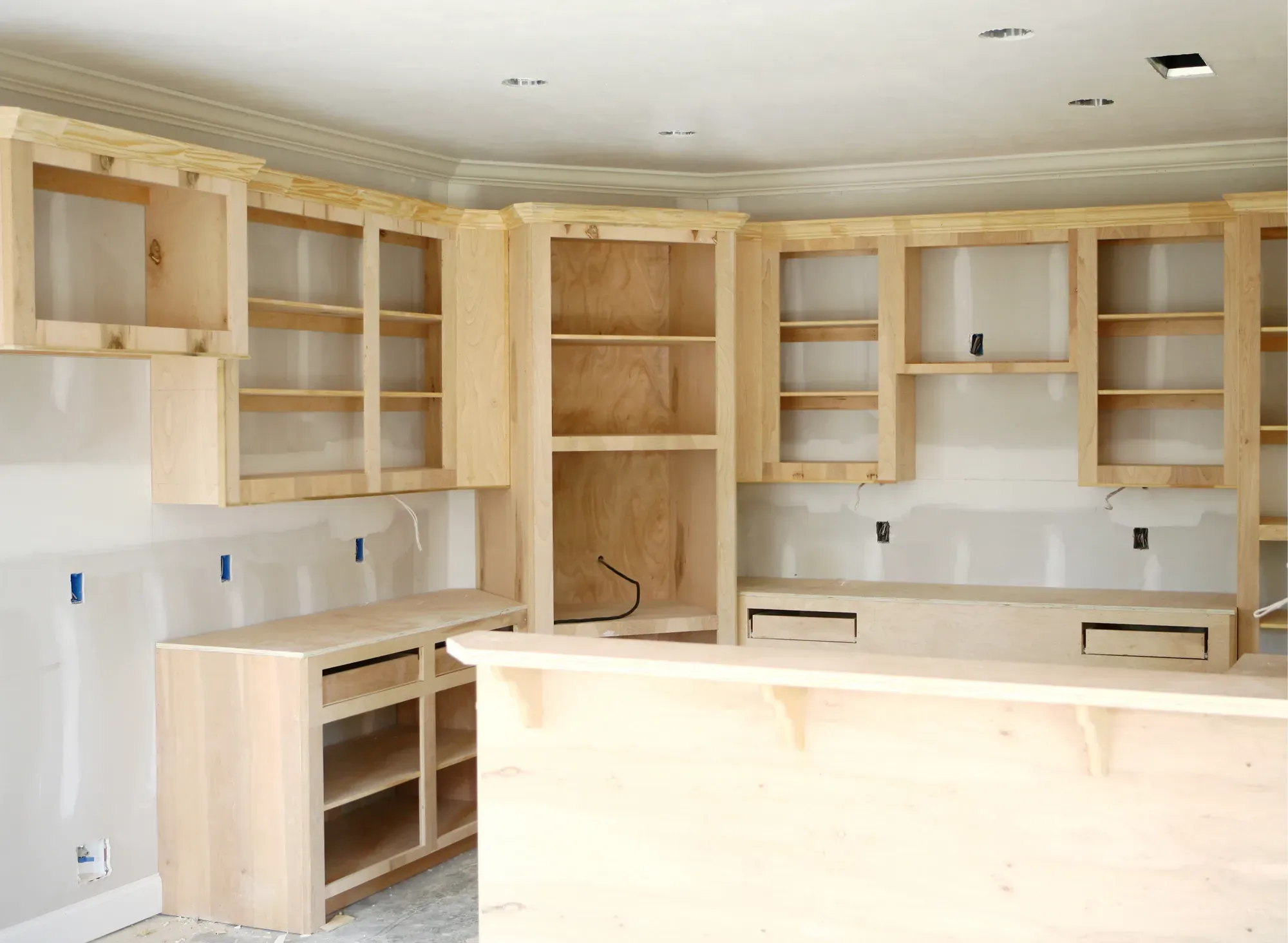 Unfinished wood cabinet boxes mounted on a kitchen wall during installation, with the doors and drawer fronts not yet fitted