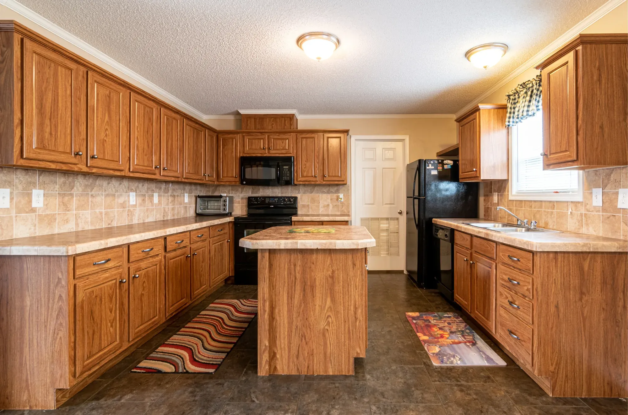 A traditional kitchen with honey-toned oak cabinets, a central island, tile backsplash and a runner rug on the floor