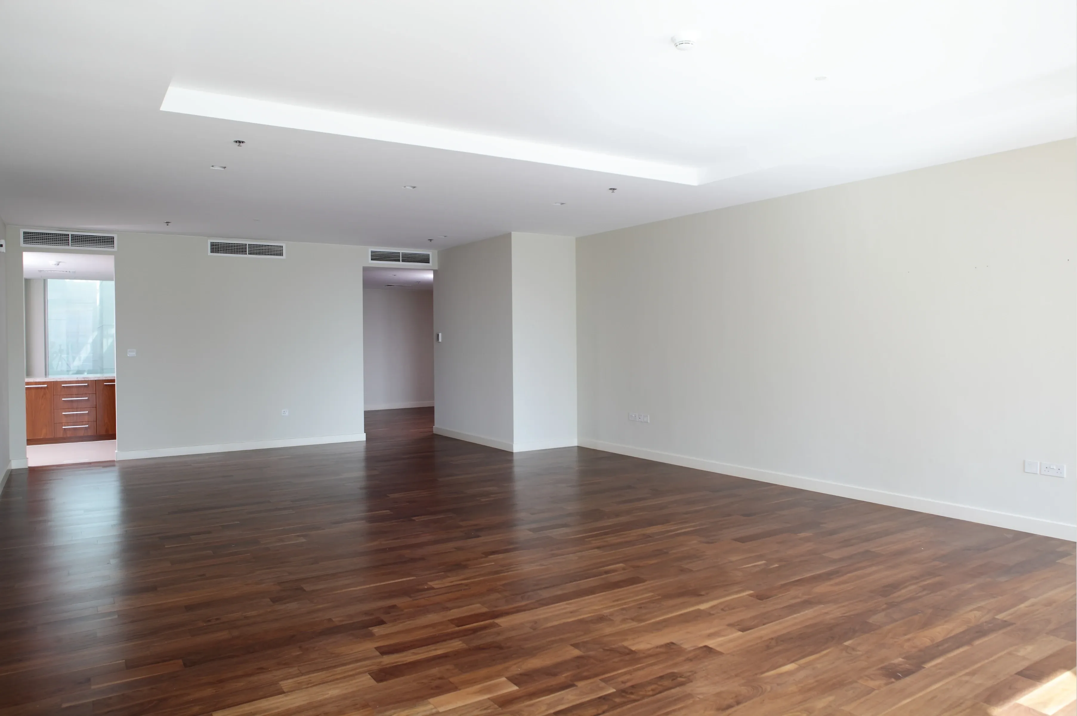 Empty apartment living area with dark hardwood flooring and bare walls, ready to hand over